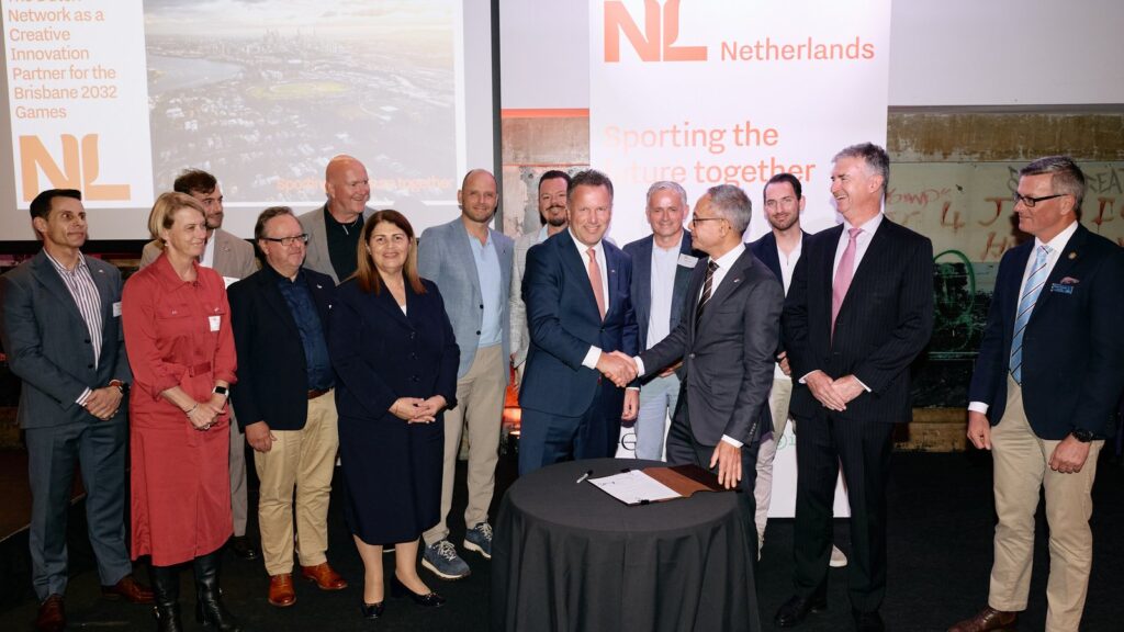Guido Tielman and Camil Smeulders shake hands after signing the Partners for International Business agreement at the Brisbane Powerhouse, with the delegation and Queensland guests gathered behind the signing table.